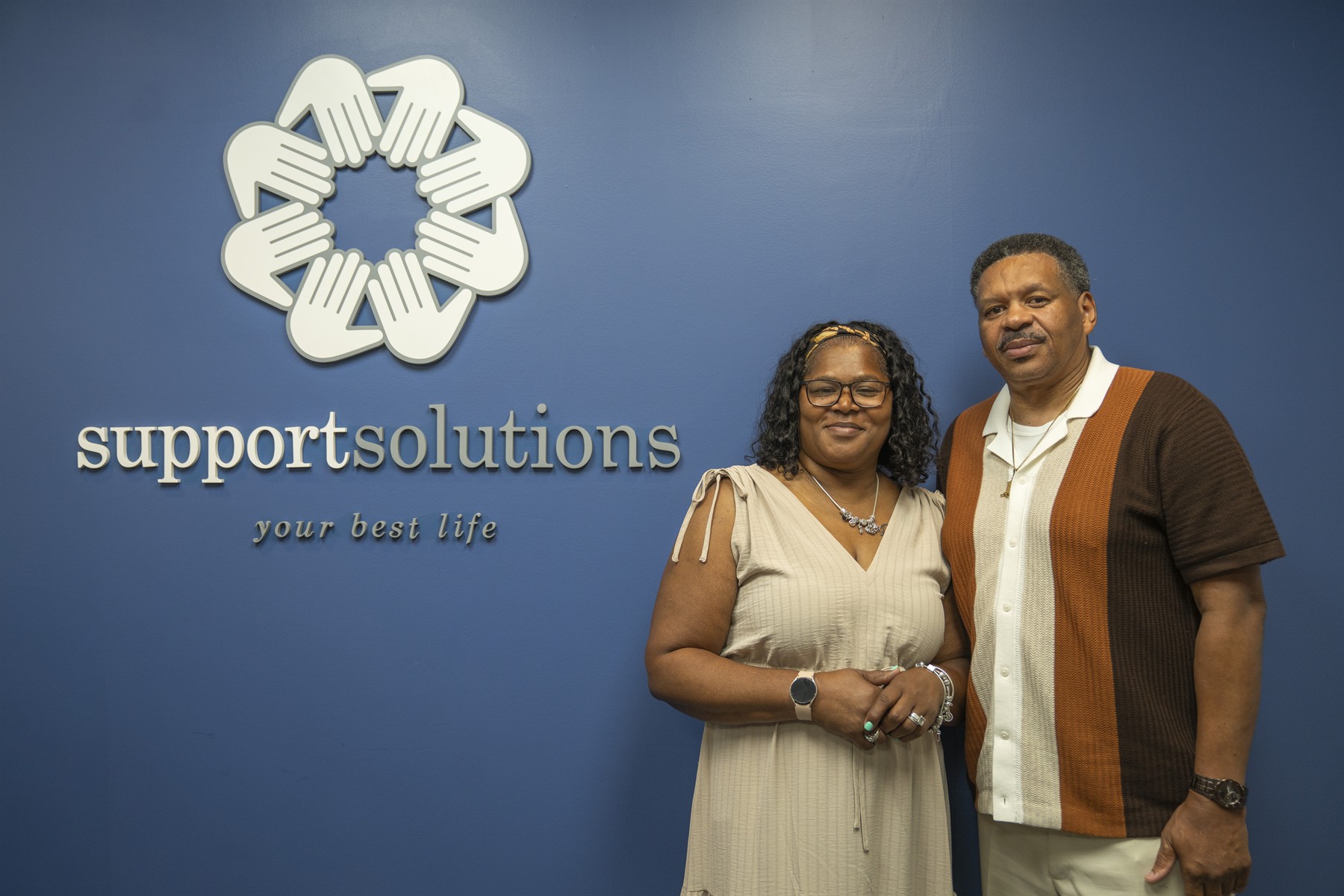 Corey Hubbard and Lisa Green standing in front of the Support Solutions wall sign